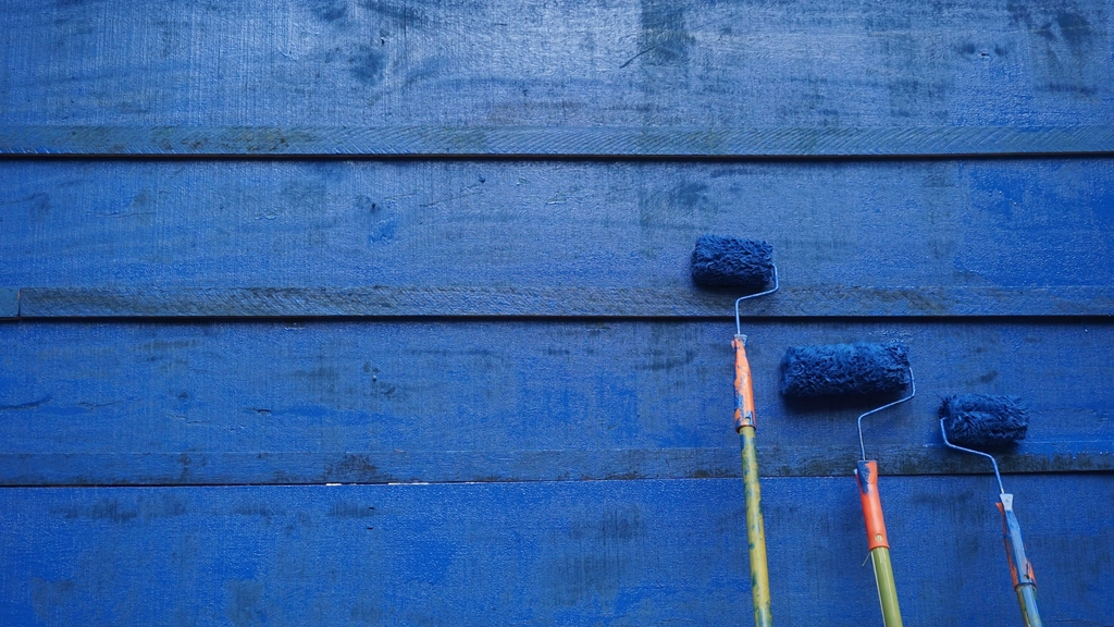 Paint rollers on freshly painted blue wood siding
